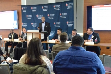 Panelists at table speaking to seated students and faculty