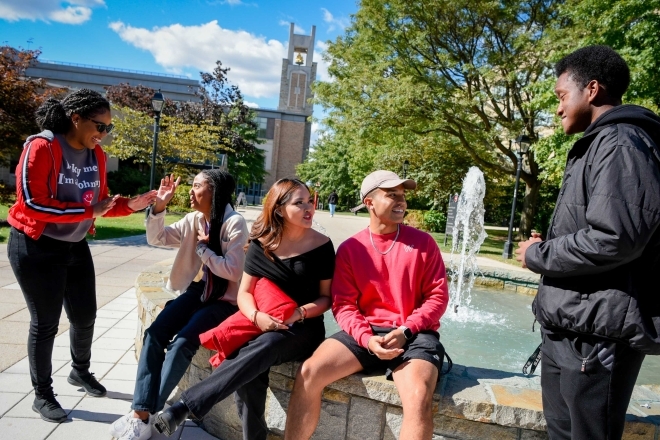 A Group of 5 students hanging outside next to a water fountain talking and laughing