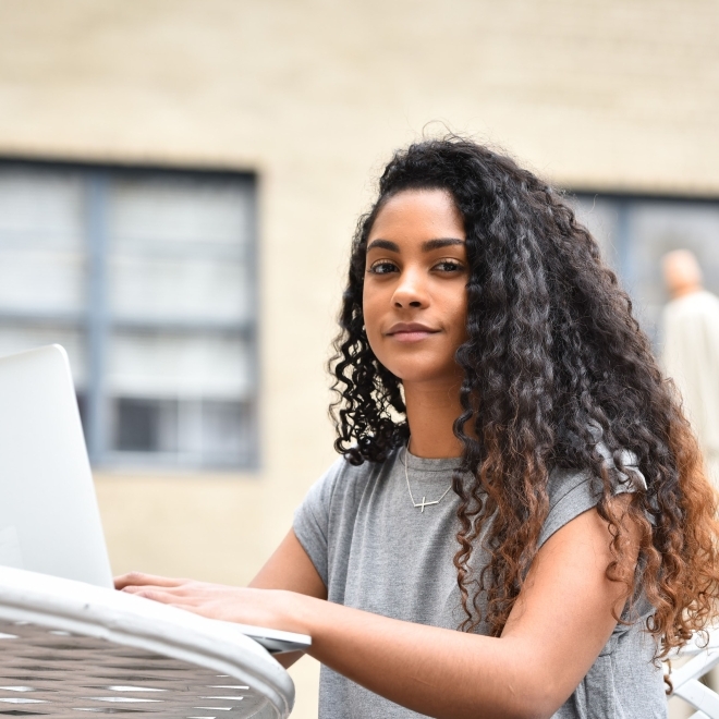 St. John’s University female student typing on laptop while sitting at a table outside.